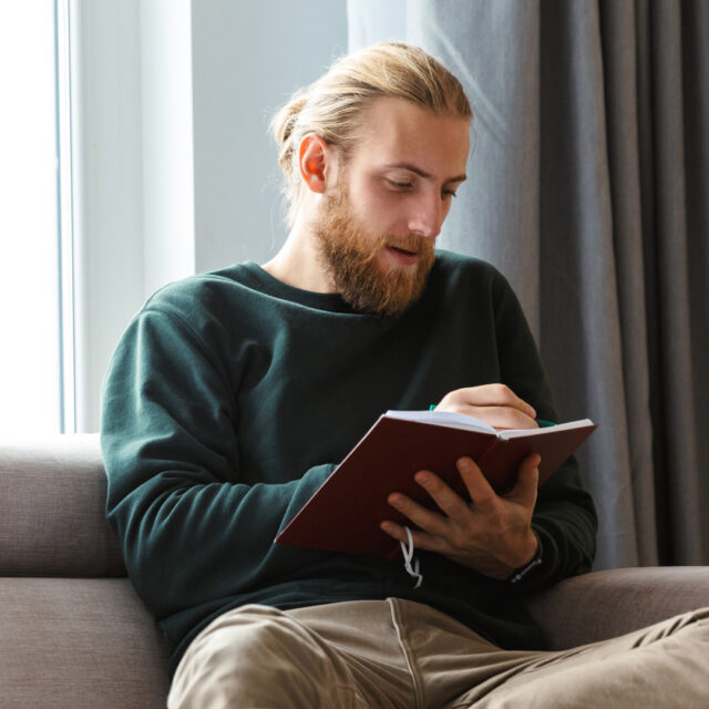 Adult learner sitting on a couch, writing in a notebook