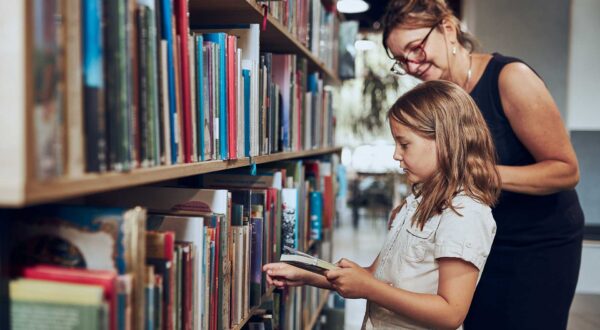 A teacher helps a child pick out a book at a school library.