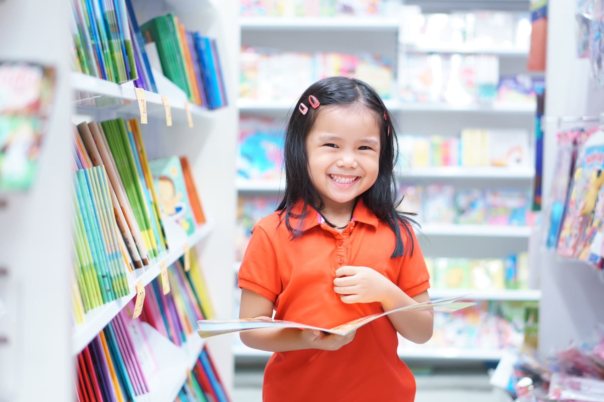 Smiling young child holding an open book in a library