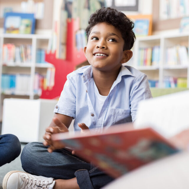 A teacher reads a book to elementary students in a library.