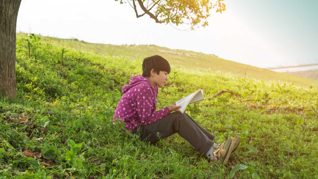 Student sits outside under a tree reading a book