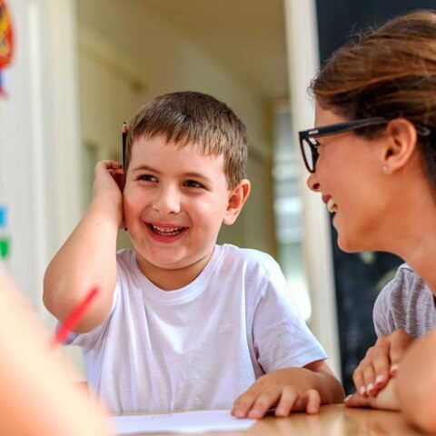 A young boy and mother seated at a table are smiling and laughing