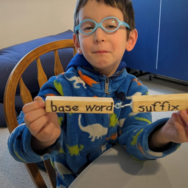 Student holds two connected wooden blocks. The first one says “base word” and the second says “suffix”